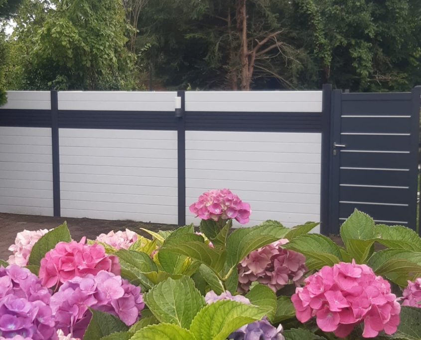 Betonzaun Modern Betonzaun, Lamellen Design mit Aluminiumtür. Der Zaun wurde in Weiss mit einer schwarzen Streife, Pfosten sind in Schwarz.